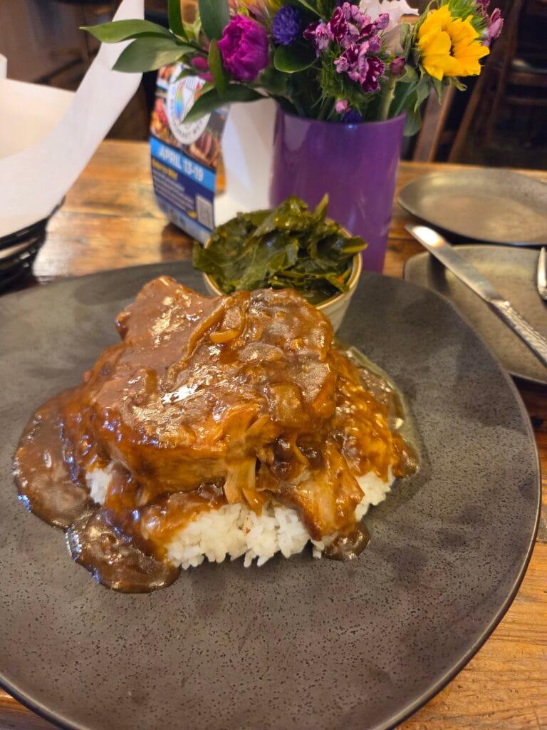 Picture of a plate containing a smothered porkchop over rice with collard greens